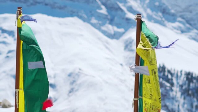 Slow motion shot of prayer flags waving in the wind in front of snowy Himalayan mountain peaks during the winter season as seen from Shashur Monastery in Keylong at Lahaul Valley in Himachal Pradesh.
