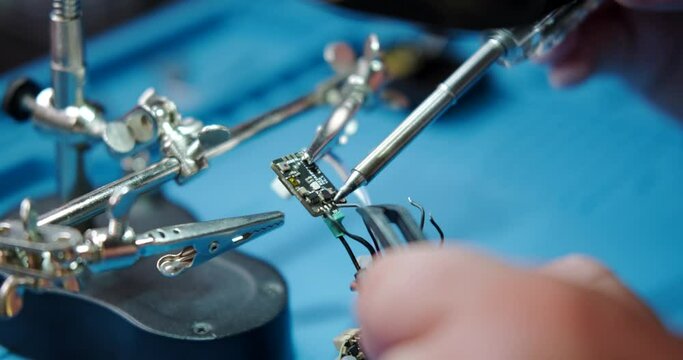 Close-up of a male engineer's hands soldering a video transmitter chip from an FPV drone using a magnifying glass. Service center for repair and maintenance of equipment. Drone repair.