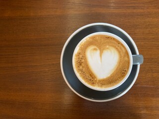 cup of hot cappuccino coffee with lovely heart shape latte art on a dark brown wooden table with the copy space on the left side of the frame