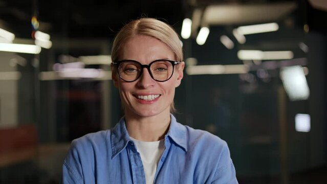 Pretty woman with beautiful facial feature standing in spacious business center. Smiling female dressed in casual attire and glasses exuding attractive and composed behave while looking at camera.