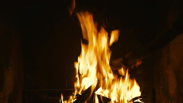 Fire in the fireplace, a man straightens the coals in the fire, natural light from a fire, 4k video, idea for a background or screensaver about home comfort, footage from a static camera
