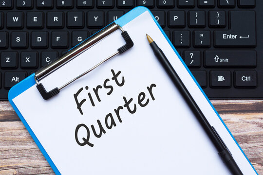 Clipboard with first quoter text with pen and keyboard on wooden desk.