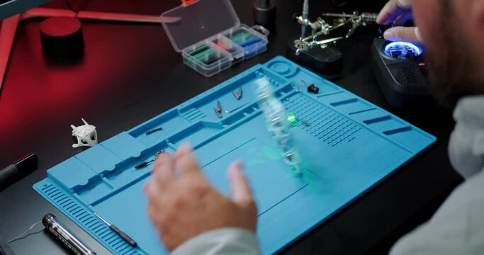 Test flight of the FPV drone after repair. A close-up of the hands of an engineer who repairs drones and checks his work. A young man is engaged in his hobby at home in the evening.
