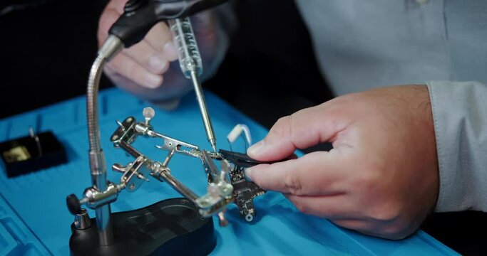 A close-up of a mans hands on a workbench where he is soldering the video transmitter chip from an FPV drone. A young engineer solders an electronic board. In the evening a man is busy with his hobby.