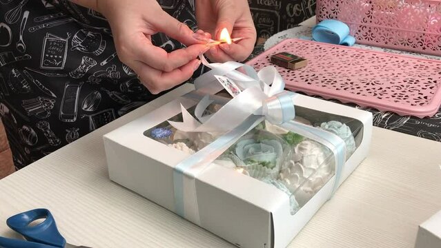 A woman burns the edges of the ribbon on a box of homemade marshmallows with a match. Zephyr flowers. A freelance entrepreneur.