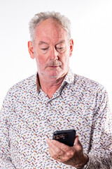 This portrait captures a senior man deeply focused on his smartphone, representing the increasing engagement of older generations with modern technology. His concentrated expression and the careful