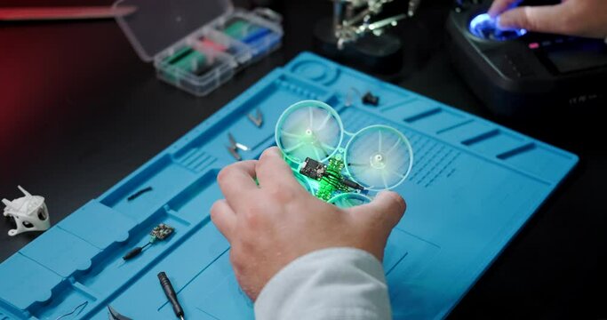 Test flight of the FPV drone after repair. A close-up of the hands of an engineer who repairs drones and checks his work. A young man is engaged in his hobby at home in the evening.