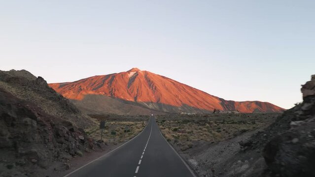 A breathtaking view of a road cutting through a serene desert landscape, with the majestic Teide mountain towering in the background.