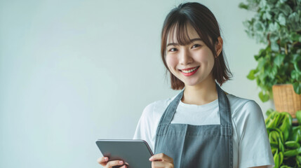Fototapeta premium young smiling welcome asian female woman business owner wear apron hand holding tablet ready for your order on white color background, restaurant, pretty, uniform
