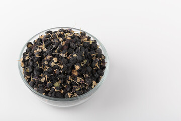 Black wolfberry or black goji berry in clear glass cup on isolated white background.