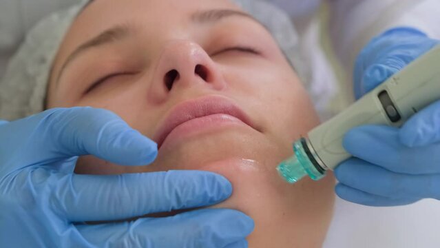 Beautician in gloves conducts vacuum cleaning and polishing face skin of young woman in cosmetology clinic. Professional hardware procedures. Hydrafacial massage process.