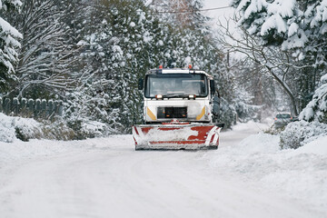 A snowplow truck applies salt and sand as the truck works to clean the snowy road. Roads and infrastructure maintenance during winter time. Rust and damage to vehicle undercarriage.