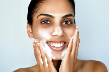 Facial cleansing. Skin care beauty portrait. Young Indian happy woman is applying foam cosmetic...