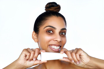 Beauty portrait of Indian beautiful woman with a hair bun is holding a tube of skin care cream or...