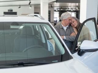 An elderly Caucasian couple chooses a new car at a car dealership.