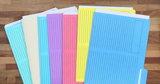 Secretary or manager puts colorful folders with accounting materials and documents on wooden table top view