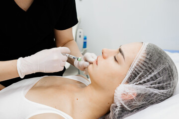 A cosmetologist makes injections into the lips of a beautiful girl. Procedure for lip augmentation,...
