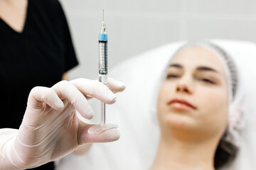 A female cosmetologist in gloves is preparing to give a young woman a cosmetological procedure. Modern dermatology clinic, cosmetic procedures and cosmetic surgery