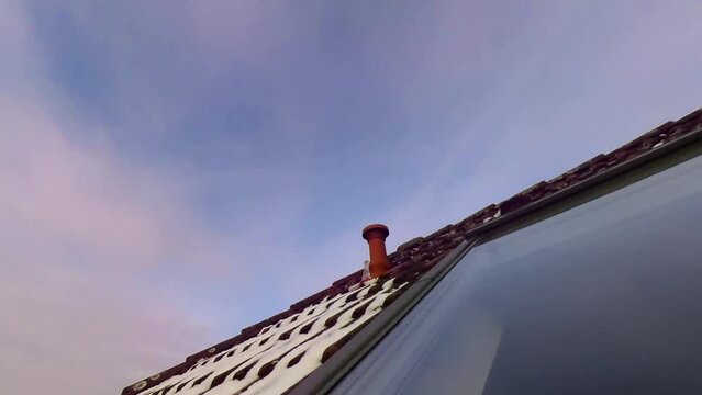 Dachfenster in verschneitem Dach mit sich spiegelnden Wolken die Abends im Zeitraffer vorbeiziehen, rote Ziegel, Dachd&auml;mmung