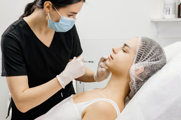 A cosmetologist wearing medical gloves performs a cosmetic procedure to enlarge the chin and...