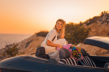 Happy beautiful blonde in a white boho style dress with a beautiful bouquet of flowers in a black...