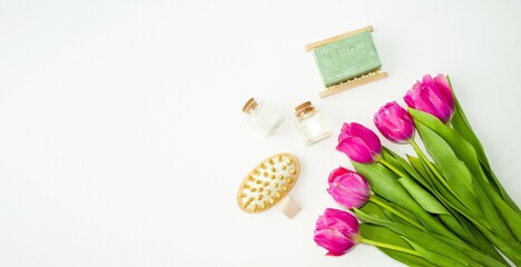 On a white background lie accessories for spa and beauty treatments, wooden brushes, aroma oils, fragrant handmade soap and a delicate, beautiful bouquet of tulips. Flat lay, top view.