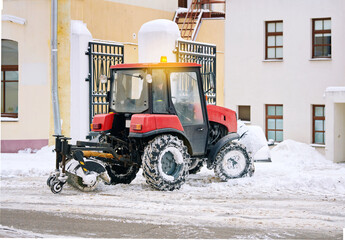 Tractor with sweeper clean snow from sidewalk in downtown. Vehicle with rotating brush and snowplow remove snow from pedestrian zone on road, sidewalk. Snow management during blizzard.