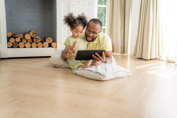 Portrait of African American father and daughter using laptop watching video, smiling while sitting...