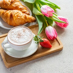 Happy mother's day, beautiful breakfast, lunch with cup of coffee (cappuccino) fresh croissants, strawberries on tray, bouquet of tulips as gift.