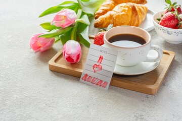 Happy mother's day, beautiful breakfast, lunch with cup of coffee (cappuccino) fresh croissants, strawberries on tray, bouquet of tulips as gift.