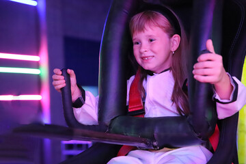 8-year-old European girl with bangs in virtual reality computer games hall on the background of ultraviolet sitting in an armchair smiling with her teeth