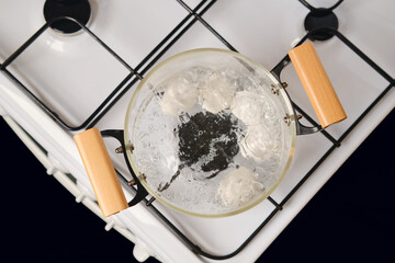Top view of glass saucepan with boiling eggs on a gas stove