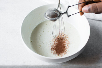 a silver strainer with Cocoa powder, sieving clumpy cocoa powder into batter