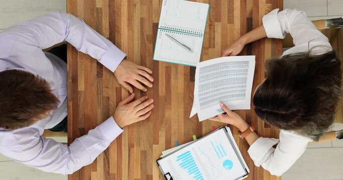 Strict female boss studying financial results in report and stressed incompetent employee top view