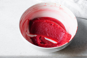 Red velvet batter in a white mixing bowl, process of making red velvet madeleines, thick red cake batter in a white ceramic bowl