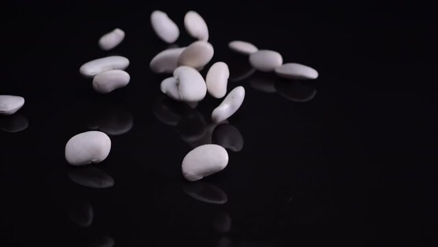 Beans tumbling slowly from glass jars onto a black, glossy surface, illustrating the use of white beans in healthy vegan recipes.