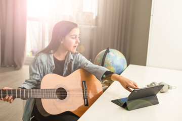 Beautiful young girl with long hair playing the guitar, sitting at home. studying the melody. Home...