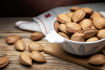 Whole almonds in shell in painted ceramic bowl on rustic wooden table, close-up. - 720069127