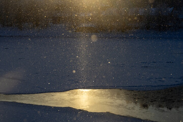 Snowflakes hit by sunrays over a patch of unfrozen water 