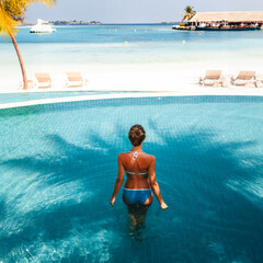 Travel vacation - Beautiful young pretty blonde girl back in bikini on her perfect sport sexy body relax in pool near paradise beach at tropical caribbean maldives beach at sunny day in hotel