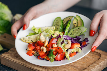 A plate with chopped fresh vegetables in female hands in the kitchen.