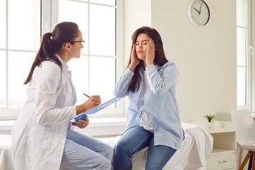 Young brunette pregnant woman visiting her gynecologist doctor in hospital or medical clinic and feel stressed, migraine and suffering from headache. Pregnancy and healthcare concept.