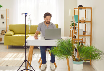 Young man in casual clothes sitting and working on laptop at the desk at home or in office while...