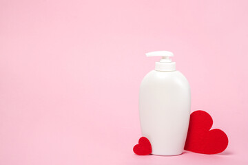 White cosmetic bottle with shampoo, soap or body lotion and red hearts on pink background, copy...