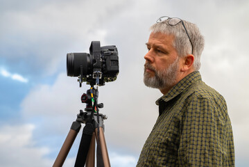 Photographer at work, gray hair and full beard, 56 years old, looking past the camera towards the...