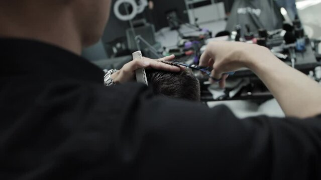 A brunette male master in a barbershop makes a haircut with scissors to a handsome young man. Modern fashionable and stylish haircut. Dynamic shooting.
