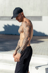 Chico joven tatuado y musculoso posando sin camiseta en la calle con ropa urbana