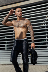 Chico joven tatuado y musculoso posando sin camiseta en la calle con ropa urbana
