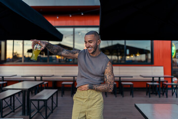 Chico joven musculado y tatuado posando con ropa urbana en terraza de restaurante de comida rapida...