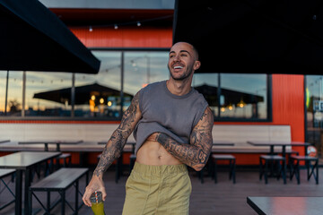 Chico joven musculado y tatuado posando con ropa urbana en terraza de restaurante de comida rapida...